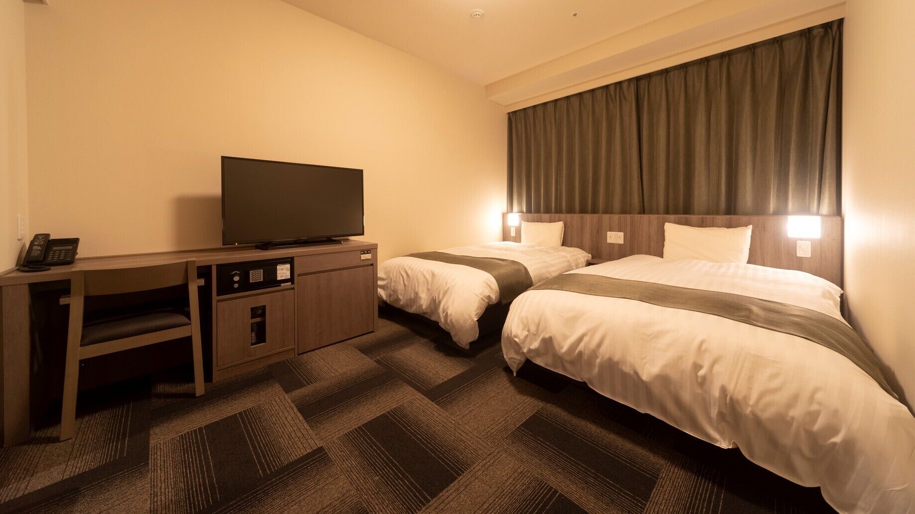 Habitación de hotel con televisión, escritorio y dos camas.
