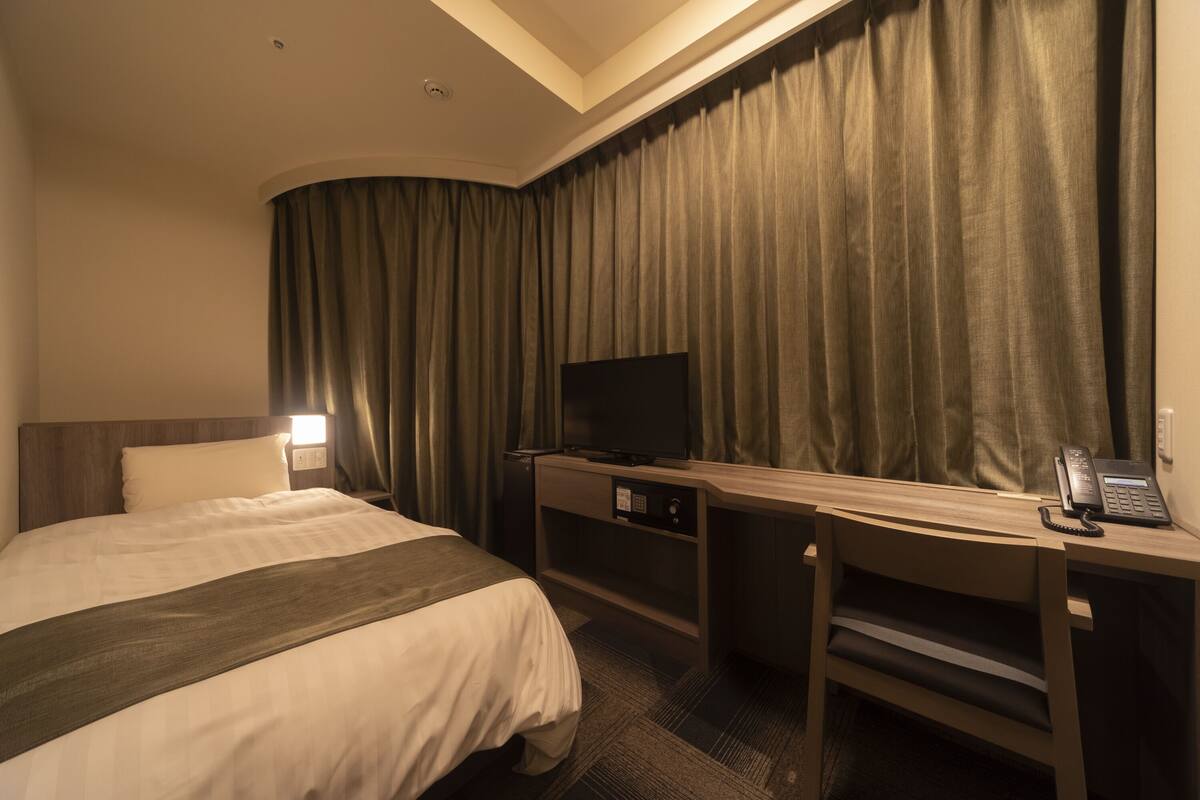 Une chambre d’hôtel comprenant un lit, un bureau avec un téléviseur à écran plat, un téléphone et un rideau.