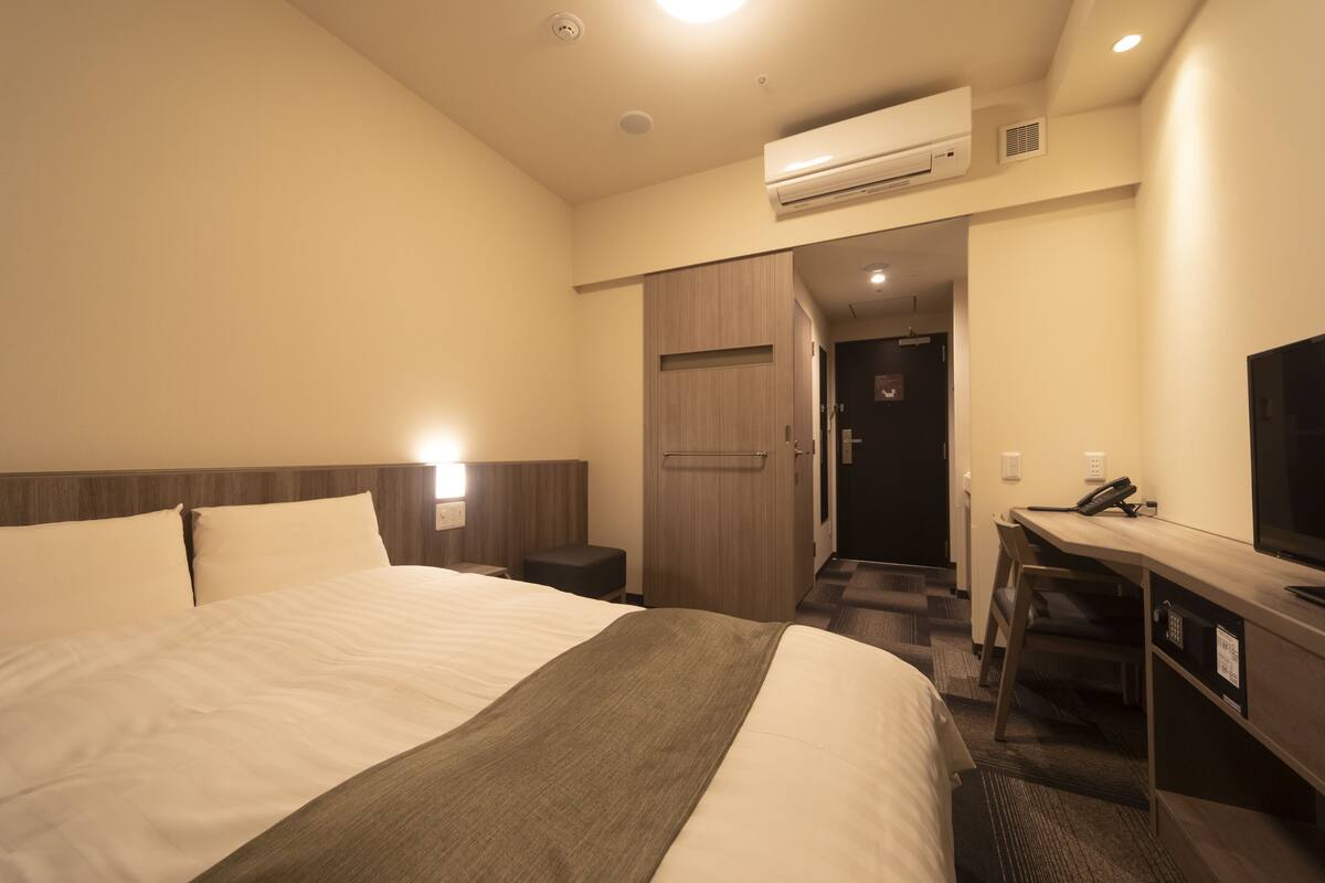 Une chambre d’hôtel avec un grand lit, un bureau avec une chaise, un appareil de climatisation et un téléviseur.