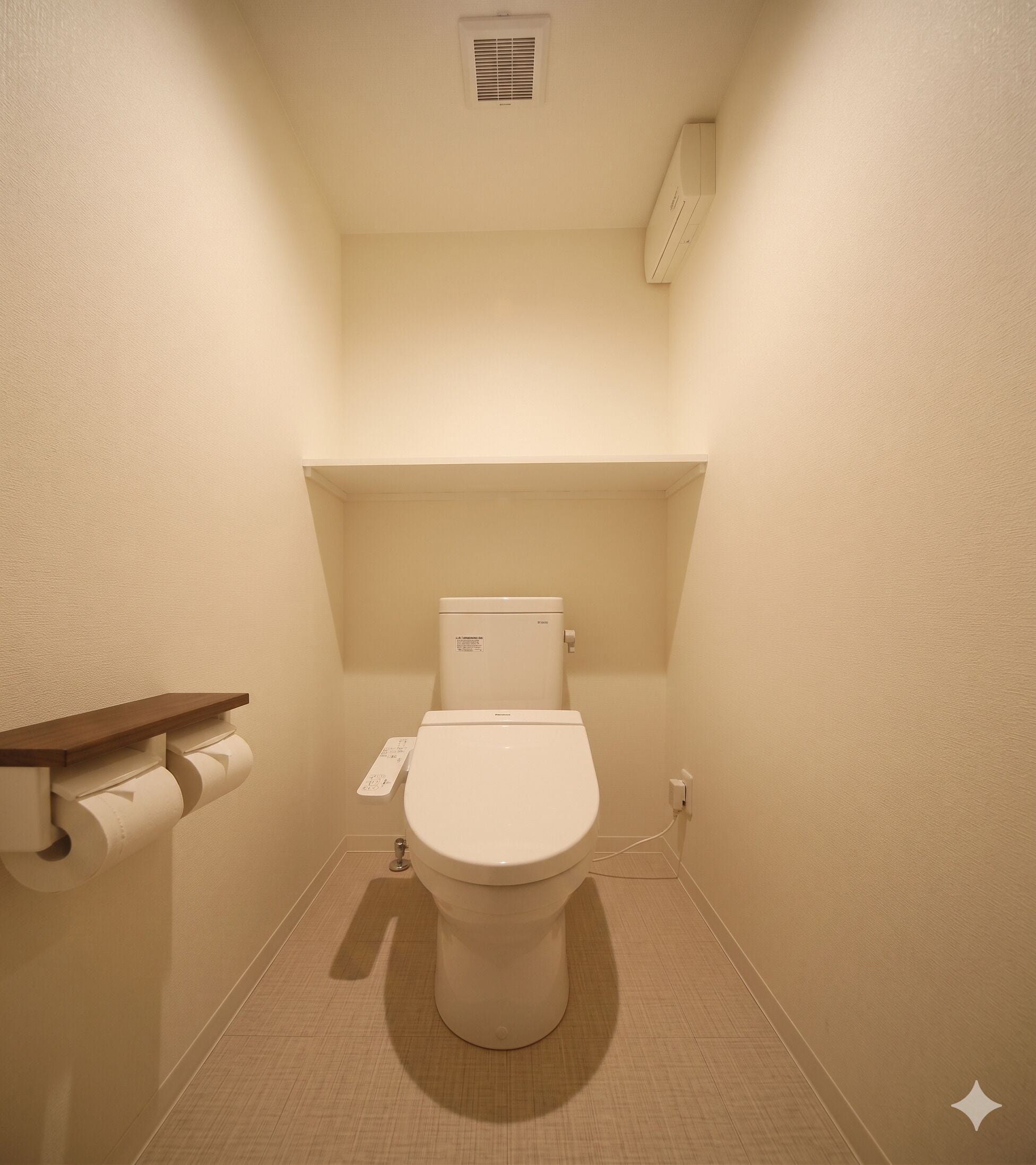 Ein kleines, sauberes Badezimmer mit Toilette, Papierhalter und einem an der Wand befestigten Ablage.