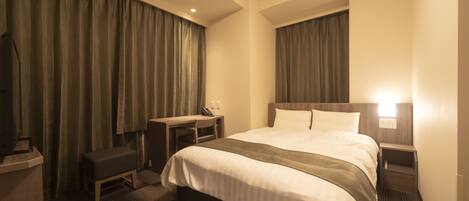 A hotel room with a large bed, a desk, a chair, a small table, and a TV.