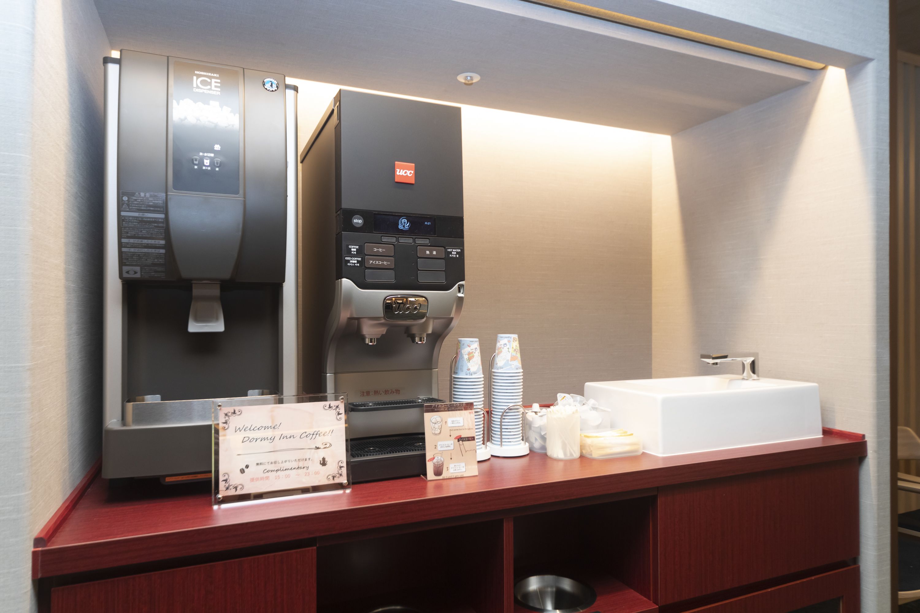 Un espace d’accueil d’hôtel comprenant une machine à café, un lavabo et un panneau indiquant aux clients la bienvenue au Doryn Inn Coffee.