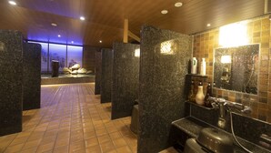 A modern bathroom with granite partitions, a tiled floor, and a shower area with a mirror and toiletries. - Dormy Inn Korakuen Hot Springs (Tokyo)