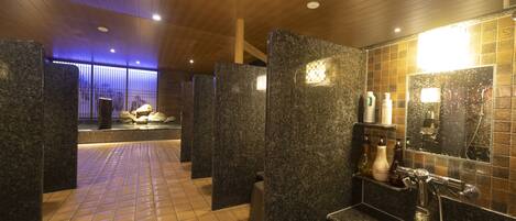 A modern bathroom with granite partitions, a tiled floor, and a shower area with a mirror and toiletries.