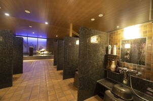 Un baño moderno con separadores de granito, piso de baldosas y zona de ducha con espejo y artículos de aseo.
