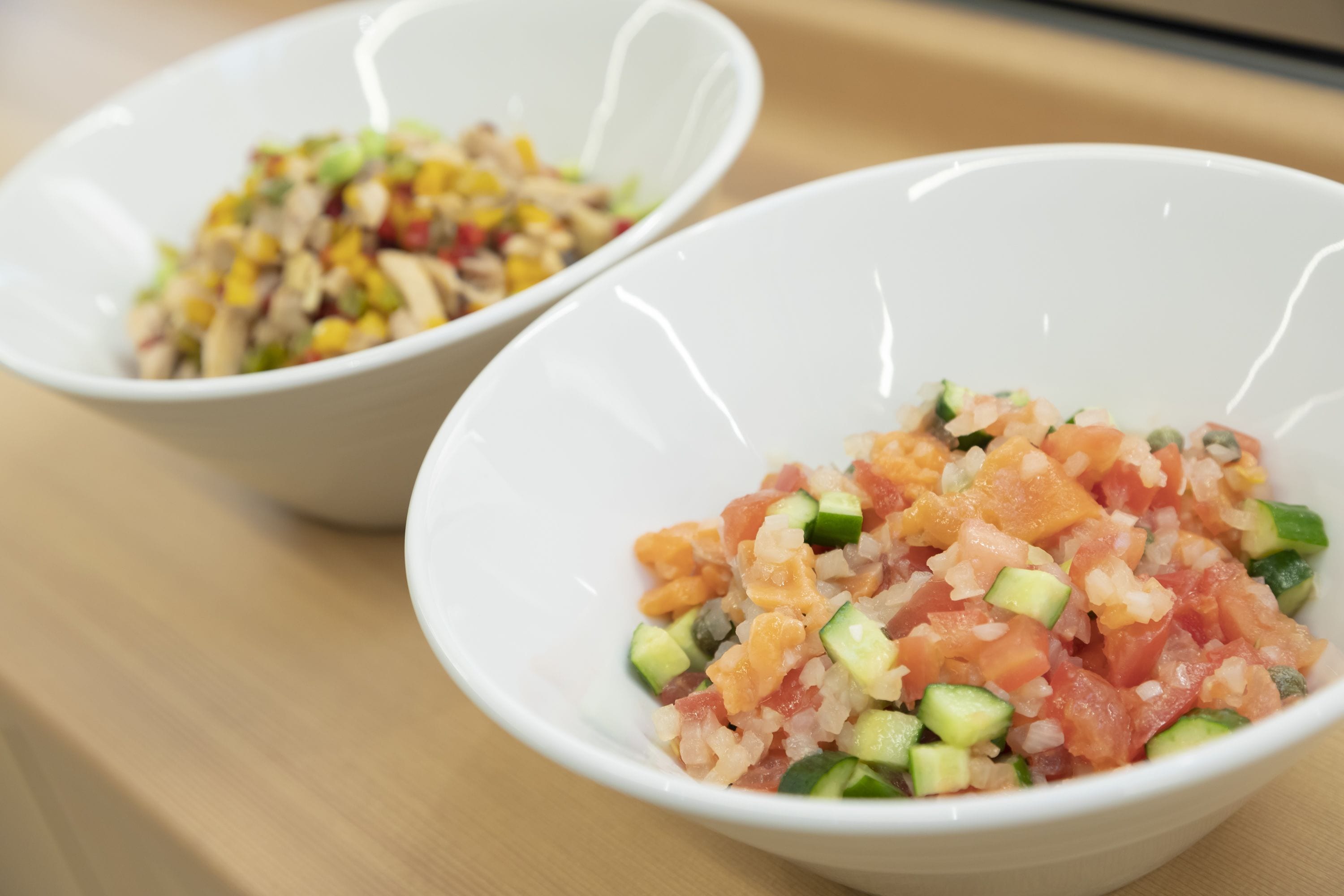 Dos tazones blancos sobre una superficie de madera, uno con una ensalada y el otro con un plato diferente.