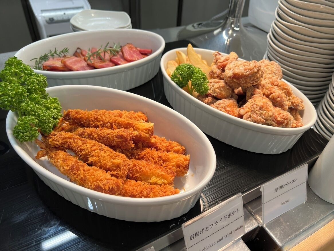 A buffet with various dishes including breaded chicken, bacon, and fried potatoes.