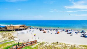 A beach with a sandy area, a wooden fence, and a building with a blue roof. - Seawind 405 | Gorgeous updates! Perfect beach view and walk to dine, shop, more! (Gulf Shores)