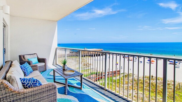A balcony with wicker furniture, a small table, and a view of the beach and ocean. - Seawind 405 | Gorgeous updates! Perfect beach view and walk to dine, shop, more! (Gulf Shores)