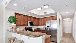 A modern kitchen with granite countertops, stainless steel appliances, wooden cabinets, and a large island with bar stools. - Seawind 405 | Gorgeous updates! Perfect beach view and walk to dine, shop, more! (Gulf Shores)
