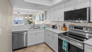 A modern kitchen with white cabinets, stainless steel appliances, and a large flat-screen TV.