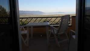 Ein Balkon mit Tisch und Stuhl, der auf eine Landschaft mit Bergen und einem Gewässer blickt.
