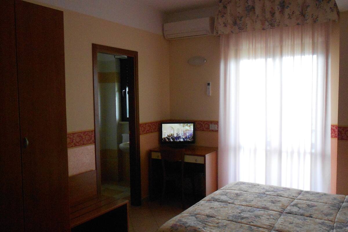 Una habitación de hotel con una cama, televisor, escritorio y espejo.