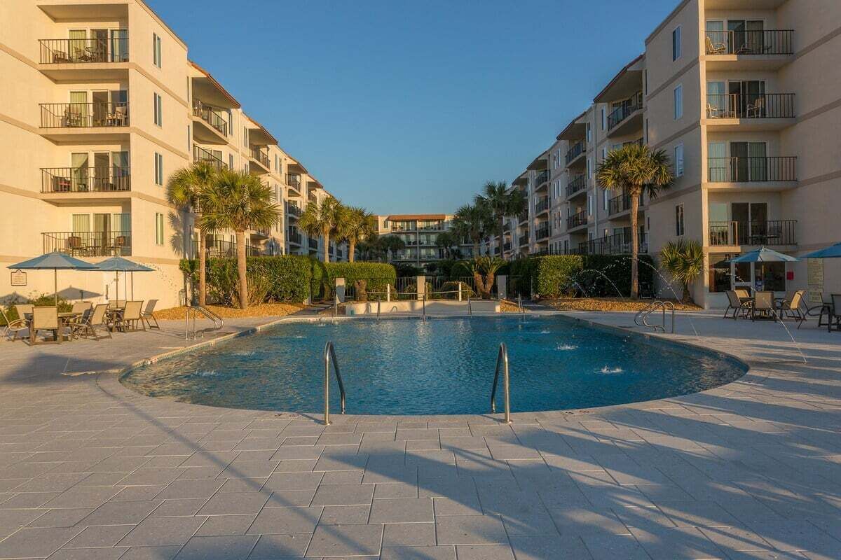 Una piscina rodeada de edificios de varios pisos con balcones, palmeras y zonas de estar al aire libre.