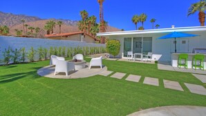 Une terrasse extérieure moderne, avec des meubles blancs, un parasol bleu et une vue sur les montagnes en arrière-plan.