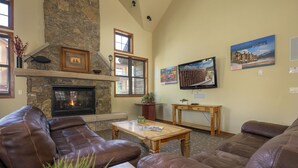 Una sala de estar acogedora con sofás de cuero, una chimenea de piedra, un televisor y obras de arte en las paredes.