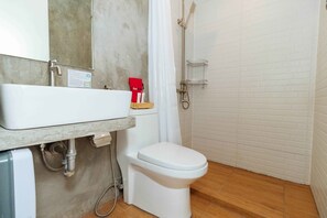 Un baño con inodoro blanco, lavamanos y zona de ducha.