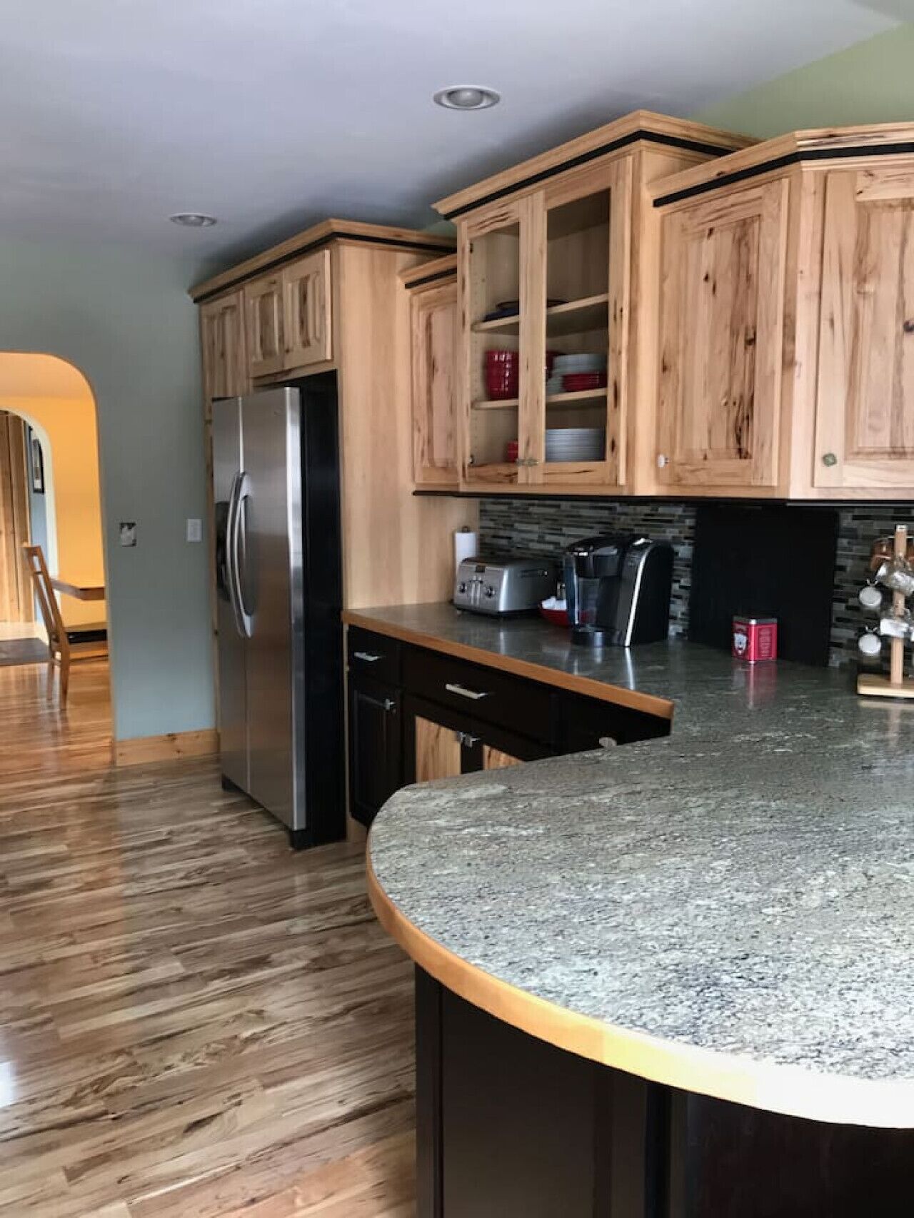 A kitchen with wooden cabinets, a stainless steel refrigerator, a granite countertop, and a toaster.