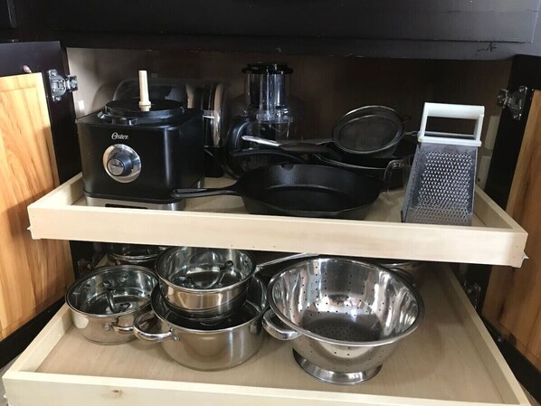 A kitchen with a black Oster food processor, a grater, and stainless steel cookware on shelves. - Happy, Healthy, Home in the Heart of Downtown BZN! (Bozeman)