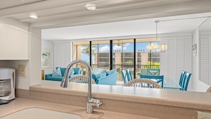 Een moderne keuken met een groot raam, een zithoek met blauw meubilair, en uitzicht op gebouwen en palmbomen.