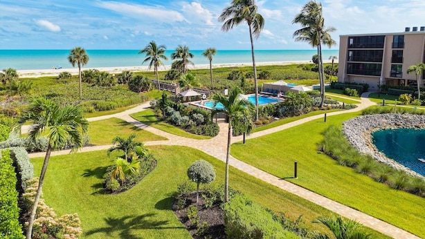 Een resort met een zwembad, palmbomen en uitzicht op het strand.