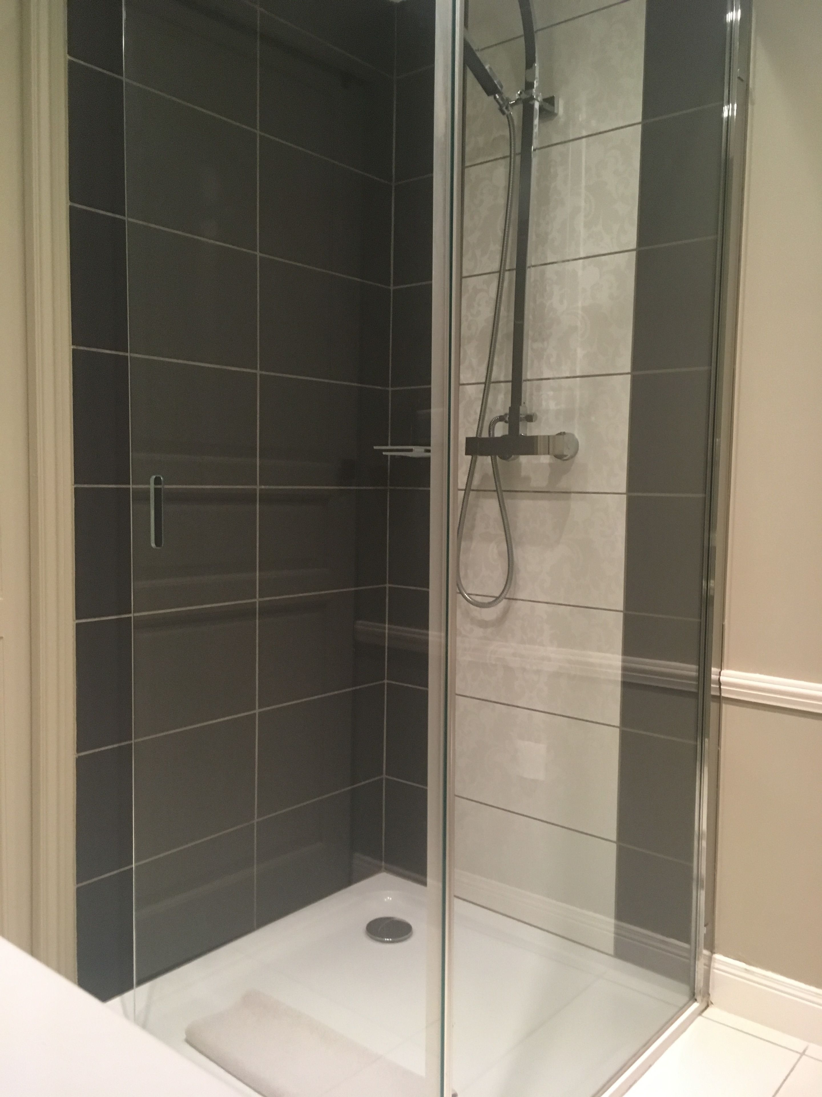 Una cabina doccia in vetro con piastrelle scure e pavimento bianco.
