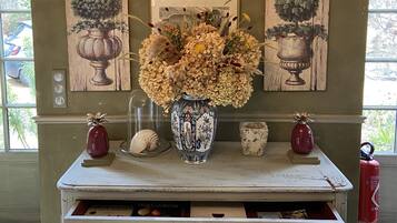 A wooden console table with a vase of dried flowers, a framed picture, and a fire extinguisher.