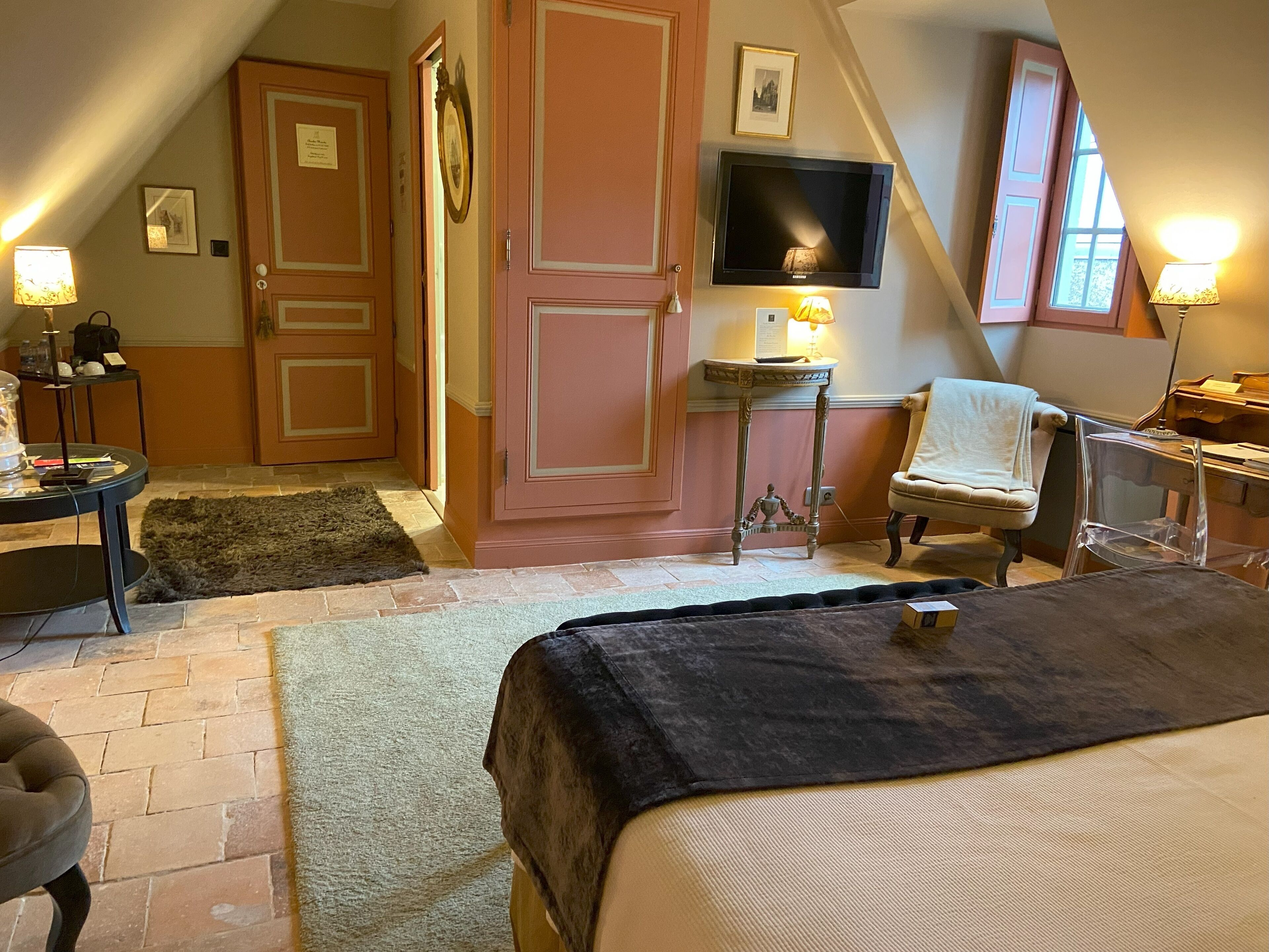 Un dormitorio acogedor con cama, una silla, un escritorio, un televisor y una puerta.