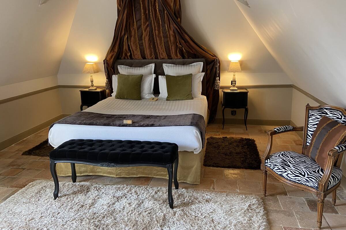Quarto com cama de dossel, duas mesas de cabeceira, uma cadeira com almofada de padrão zebra e um tapete fofo.