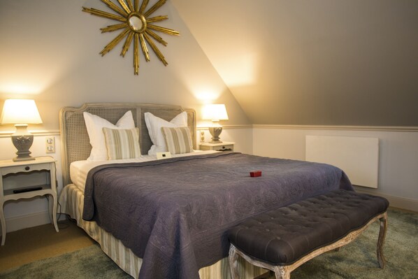 A bedroom with a large bed, two bedside tables, a bench, a decorative wall piece, and a radiator. - Manoir de Maucartier (Monnaie)