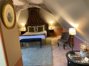 Ein Schlafzimmer mit einem großen Bett, einer Bank, einem Sessel, einem Nachttisch mit Lampe und einem gerahmten Bild an der Wand.