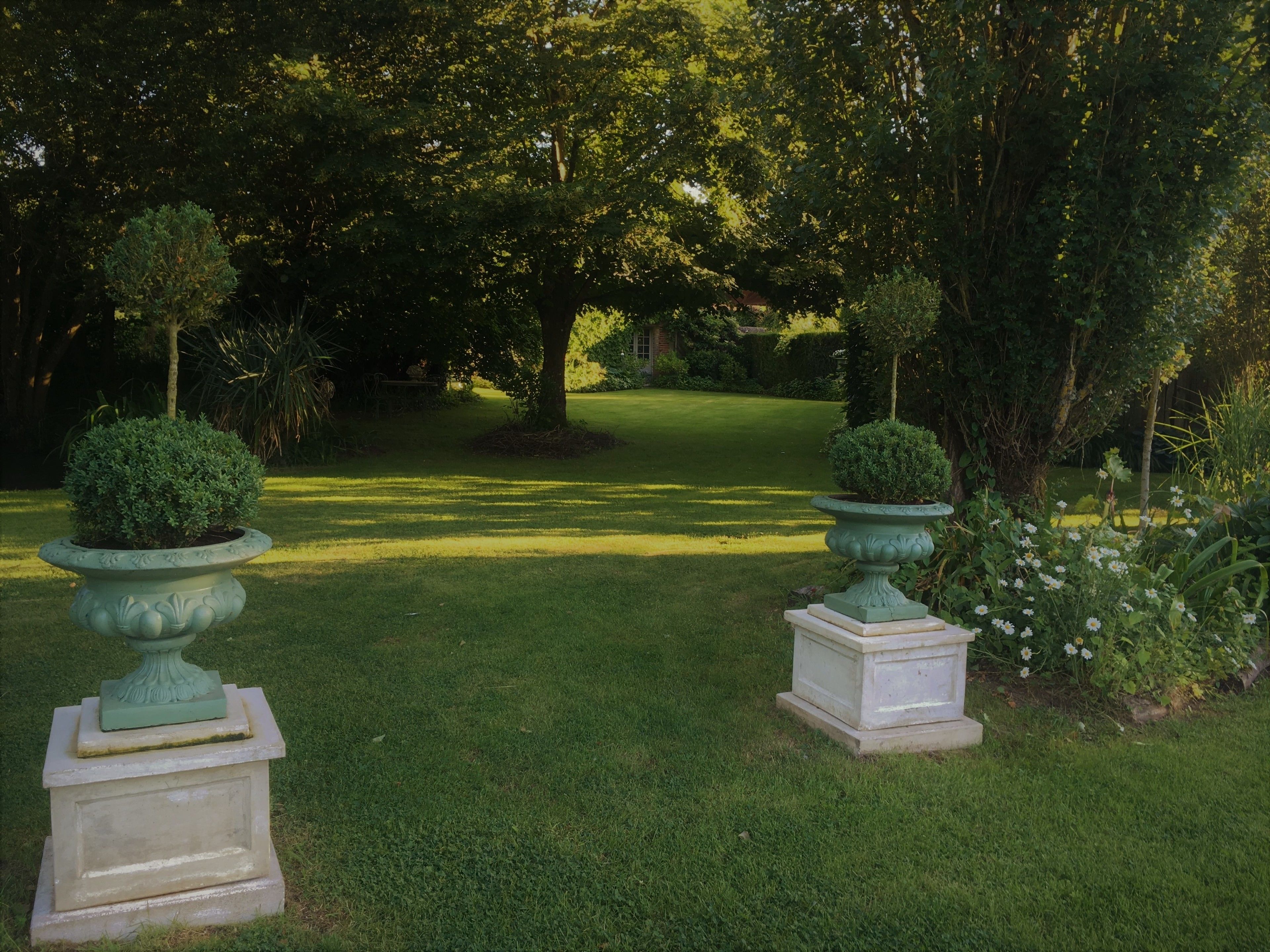A well-maintained garden with two ornate planters, a neatly trimmed lawn, and a variety of trees and shrubs.