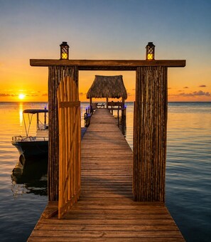 A wooden pier leading to a thatched-roof structure with lanterns on either end, overlooking calm waters at sunset. - Starfish Beach House  2BR Beachfront Retreat with Pool & Dock (Milton Bight)