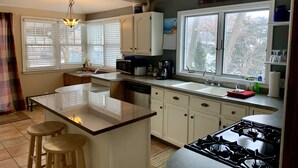 A kitchen with a central island, a stove, a sink, and a window with blinds.