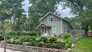 A single-story house with a front porch, surrounded by a garden with various plants and a stone border.