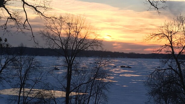 A winter landscape with a frozen lake, bare trees, and a bench.