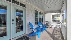 Une véranda couverte avec un plancher en bois, un ensemble de chaises Adirondack bleues et une petite table.