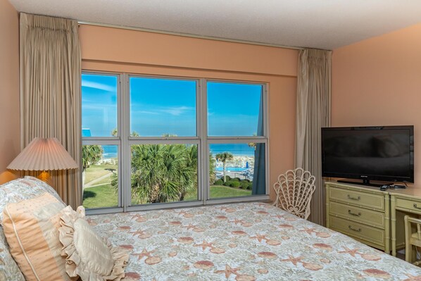 A bedroom with a large window, a bed, a TV, and a desk.