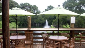 A wooden deck with round tables and chairs, green umbrellas, and a view of a waterfall.