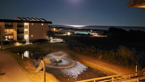 A nighttime view of a building with multiple floors, a pool, and a fountain.