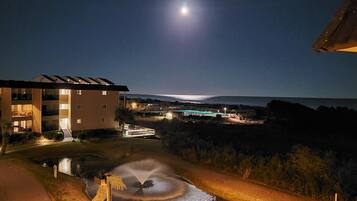 A nighttime view of a building with multiple floors, a pool, and a fountain.