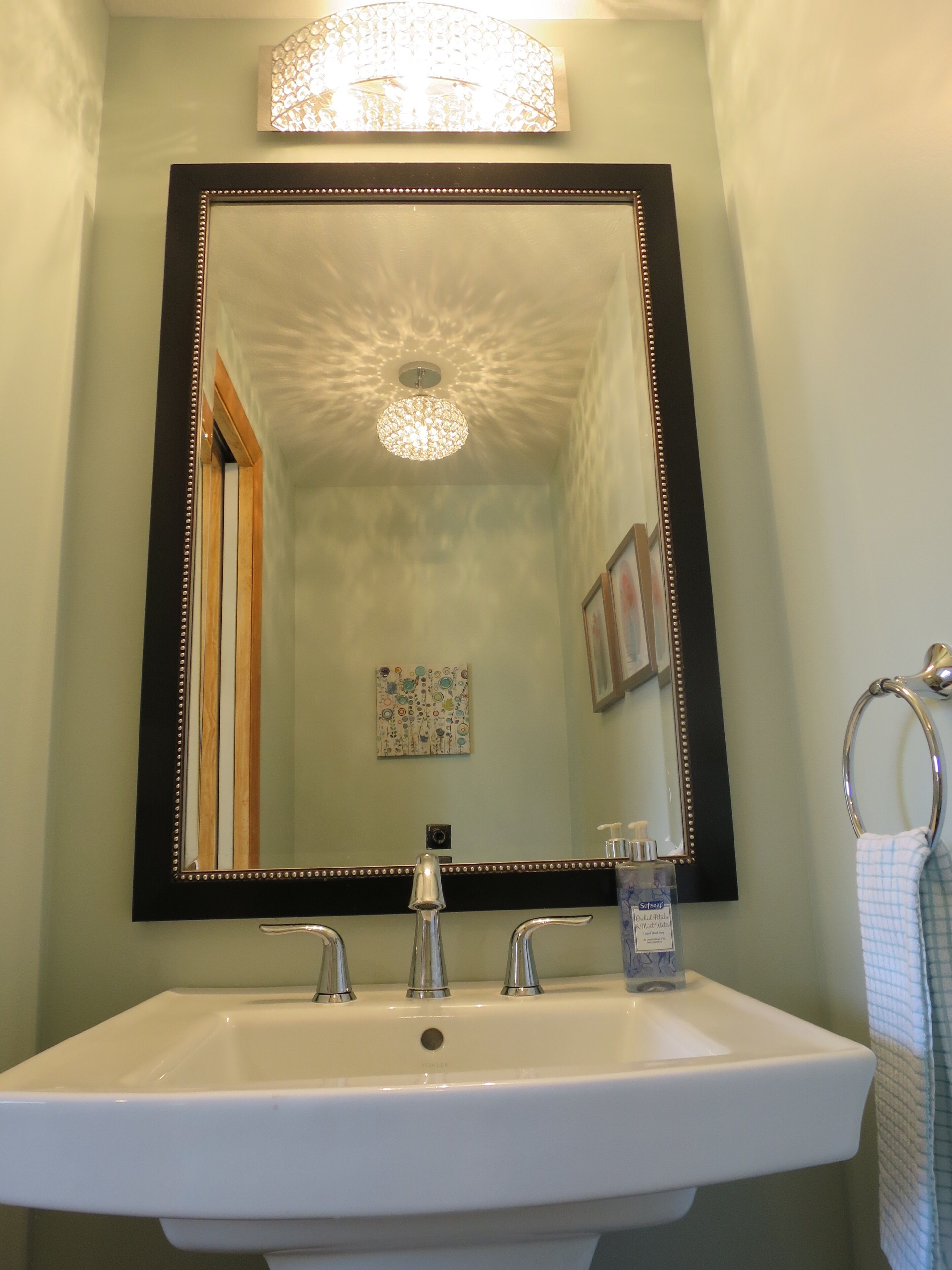 A bathroom with a large mirror, a sink with two faucets, a soap dispenser, and a towel ring.