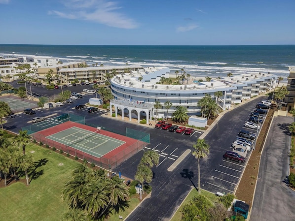 A coastal hotel with a circular building, a tennis court, and a parking lot.