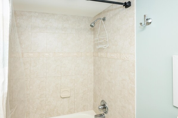 Une salle de bain carrelée de carreaux beiges, une douche avec un pommeau de douche amovible, un porte-serviettes et un distributeur de savon.