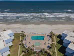 An aerial view of a beachfront hotel with a swimming pool, beachside lounge chairs, and palm trees.