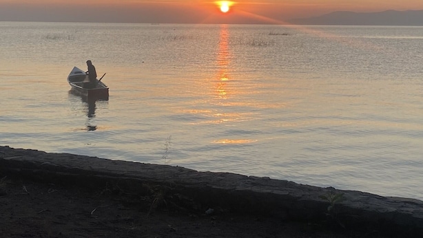 A sunset over a calm sea with a boat and rocky shoreline.