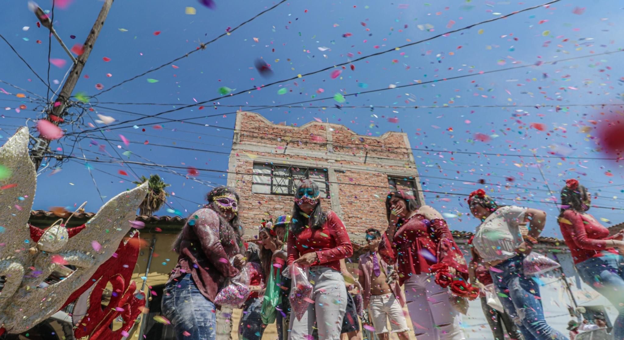 Un groupe de personnes fait la fête en lançant des confettis et en agitant des serpentins devant un bâtiment en briques.