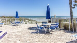 Une terrasse extérieure avec des chaises et des parasols bleus, un sol en briques et une vue sur l’océan.