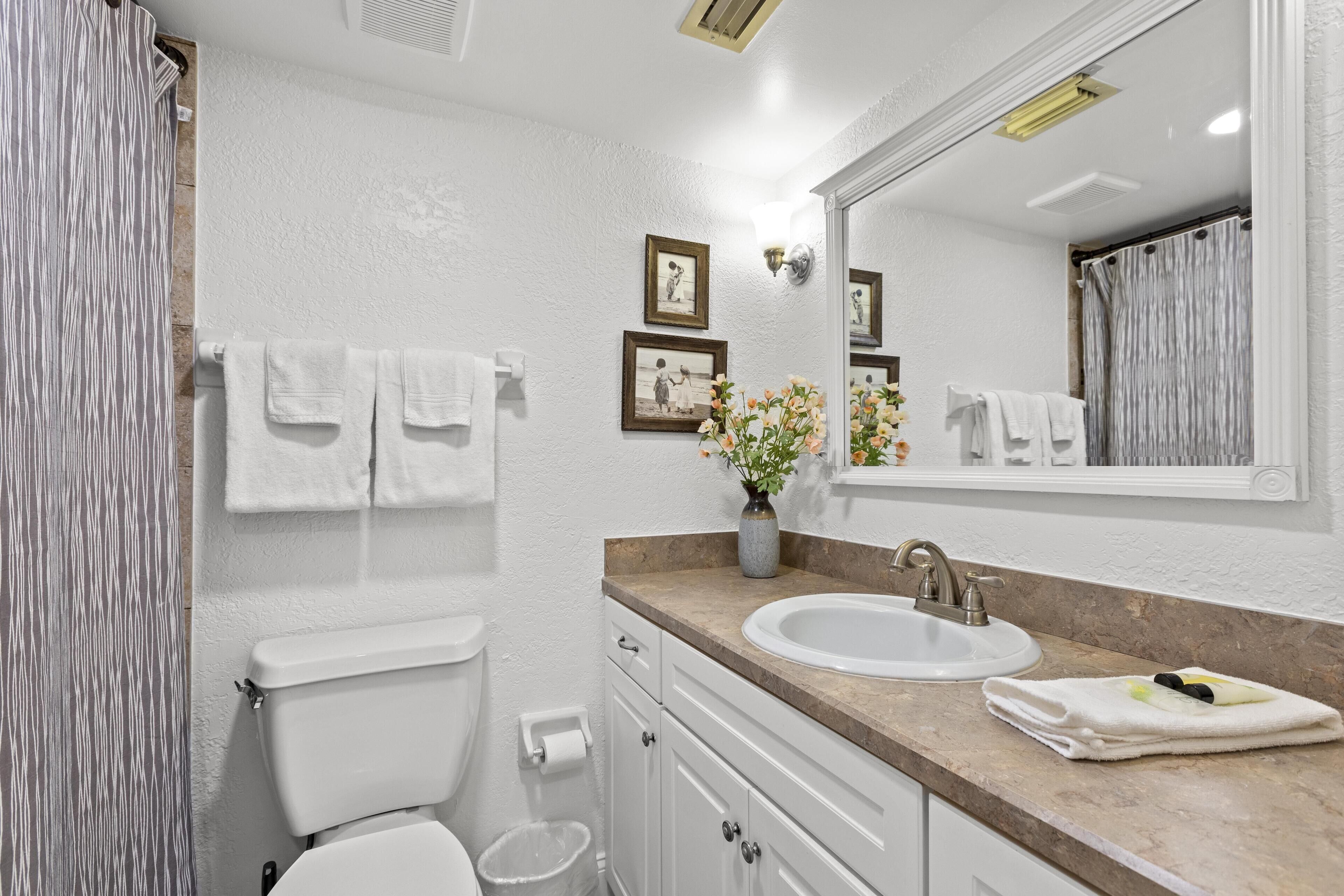 A bathroom with a toilet, sink, and mirror. There are towels hanging on the wall and a vase with flowers on the sink counter.