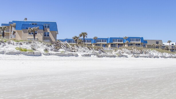 Un hôtel situé en bord de mer, avec plusieurs bâtiments bleus, des palmiers et une plage de sable.